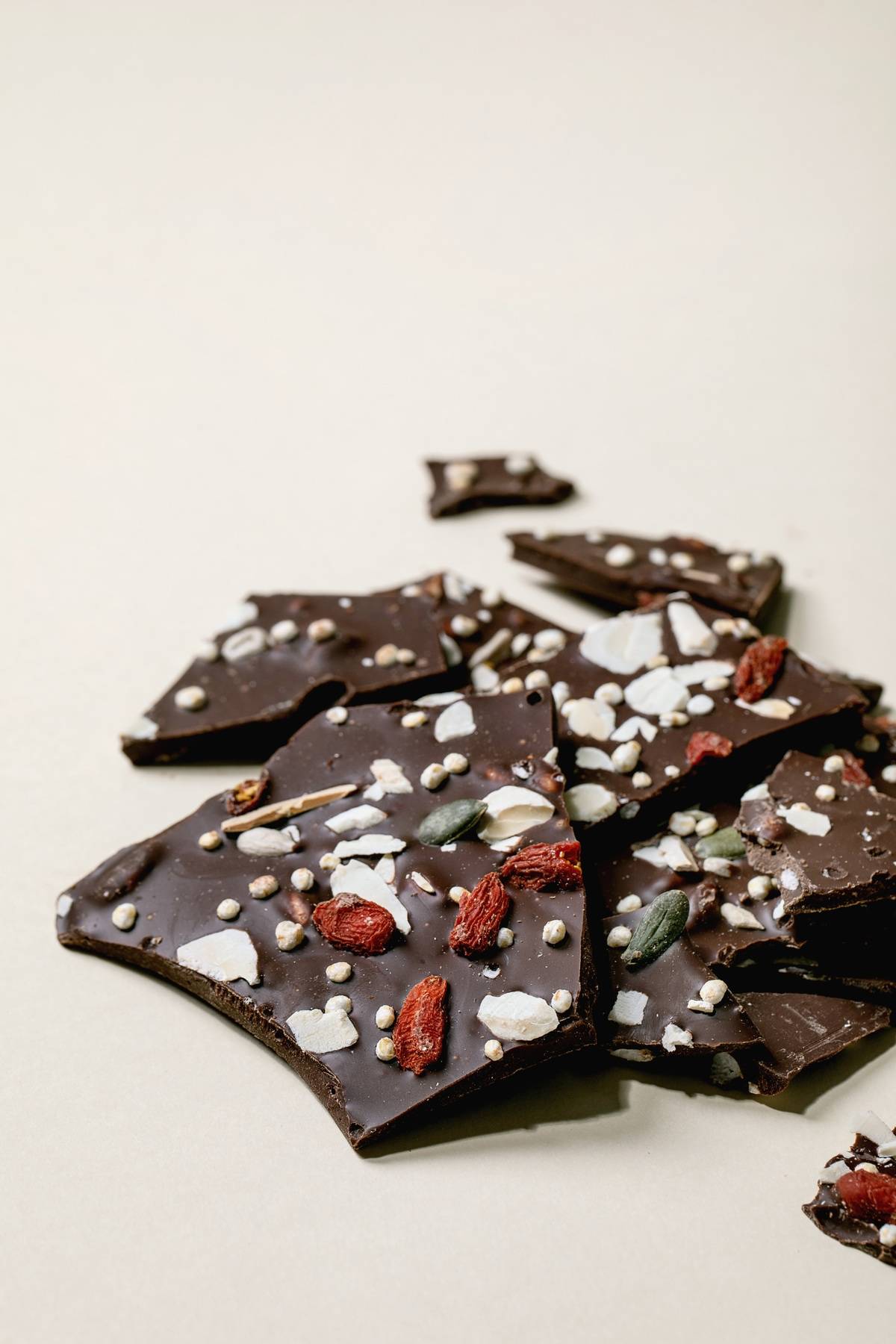 Handmade chopped dark chocolate with different superfood additives seeds and goji berries over beige background.